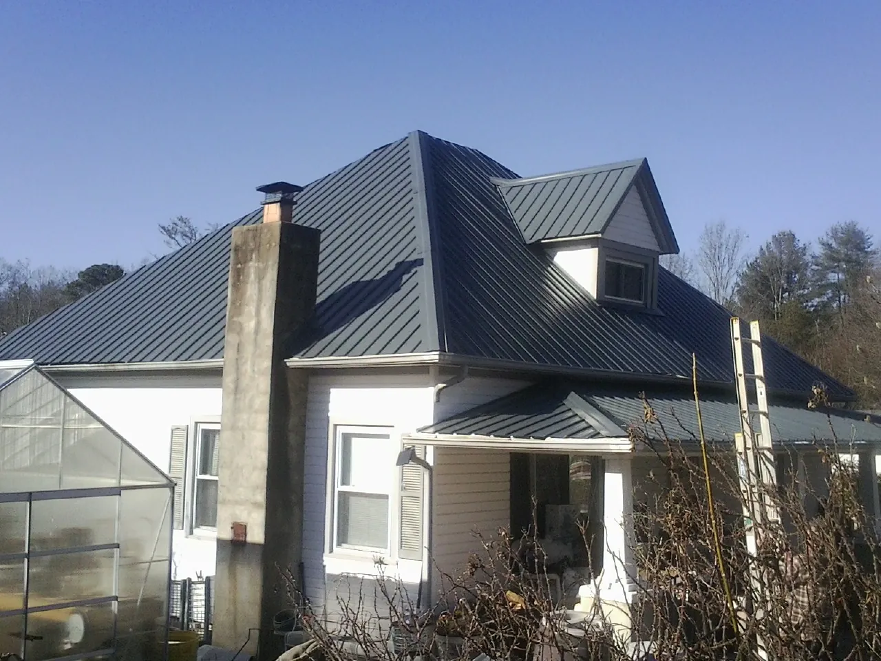 Dark blue standing seam metal roof on a white farmhouse with dormer in Hilliards