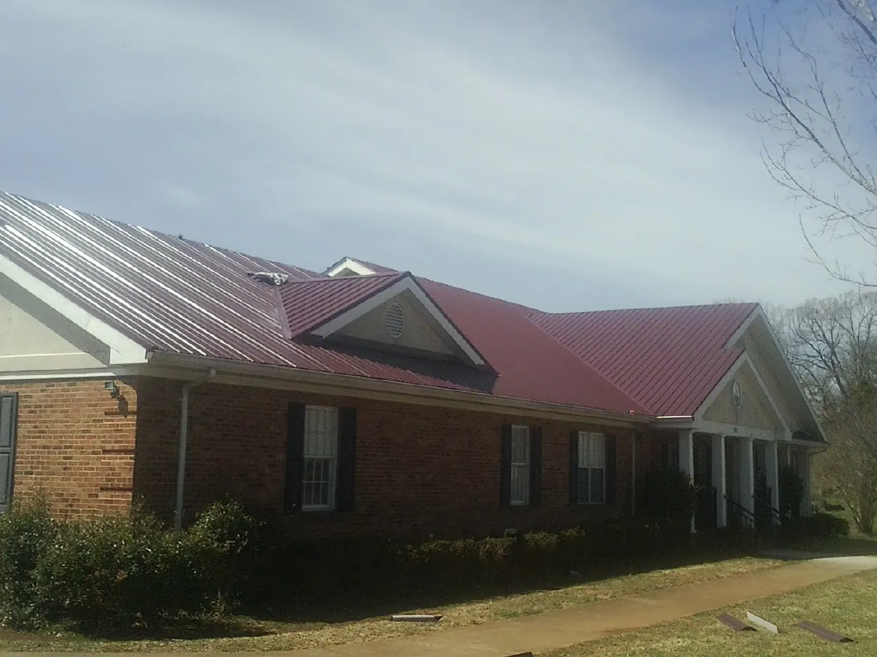 Red metal roof with gabled entries on a long brick building, from a Hail Damage Roof Repair job in Hilliards