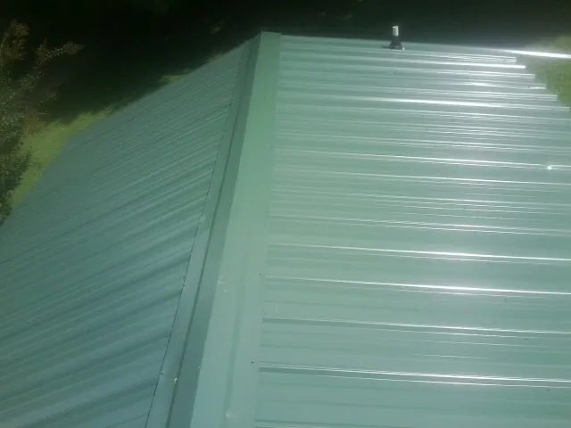 New green metal panels meeting at the ridge of a roof — Flat Roof Repair work by our crew in Hilliards