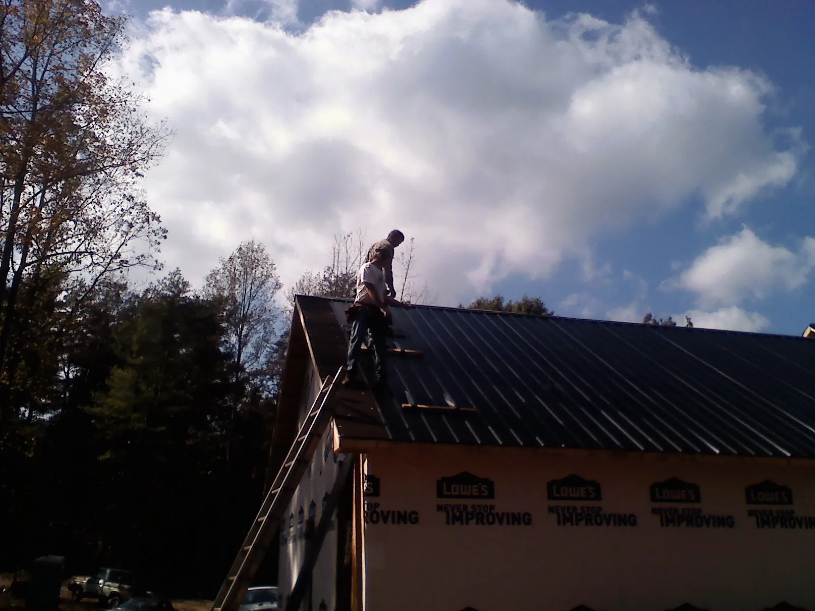 Roofer fastening dark metal panels high against a cloudy sky, from a Roof Inspection job in Hilliards